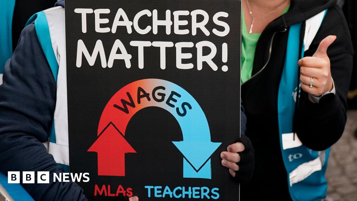 A close-up of a sign being held by teachers who are at a protest. The sign says 'Teachers Matter!' and shows a graphic indicating that wages for Northern Ireland assembly members are going up while teachers wages go down. Around the sign we can see the torsos of two people who are both wearing hi-visibility jackets. The person on the right is giving a thumbs up.