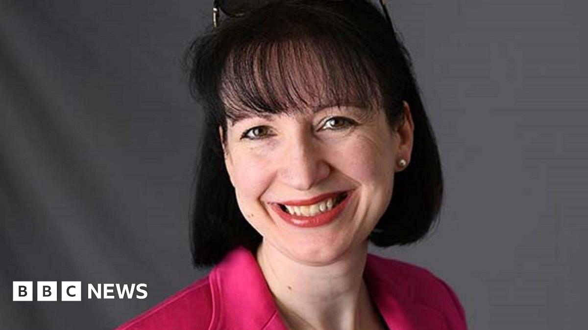 Suzy Lishman with short black hair, wearing a pink jacket, smiling for camera.