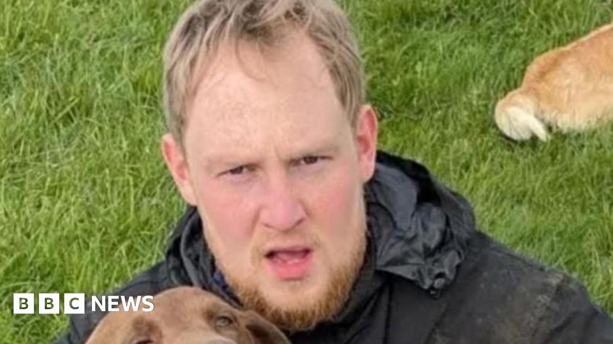 Police mugshot of Rhys Jamieson. He has a droopy left eye, scruffy hair and beard, grey t-shirt