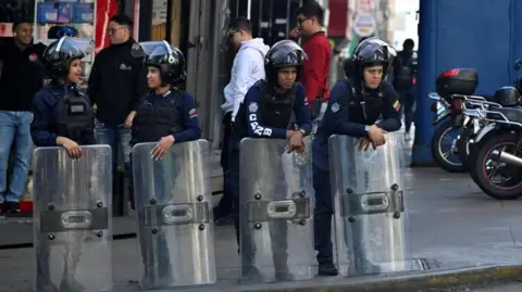 Reuters Police officers stand guard near the National Assembly in Venezuela's capital, Caracas. They are chatting to one another while wearing helmets and holding large shields.