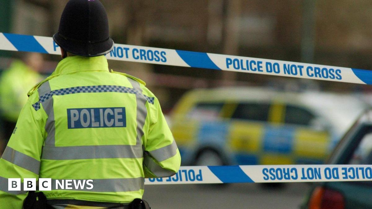 A police officer wearing a yellow jacket standing in front of a police cordon