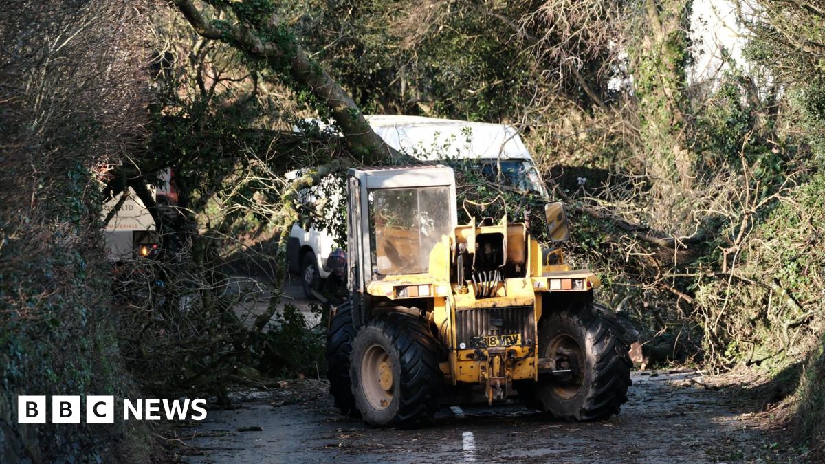 Millie Bobby Brown and David Harbour in character as Eleven and Jim Hopper. Eleven wears red shorts over grey leggings and a grey jumper. Jim Hopper wears a black leather jacket, a black beanie hat and dark trousers.They are speaking to director Frank Darabont on the set of Stranger Things. There is a vintage advertisement posted in the background with debrief on the ground.