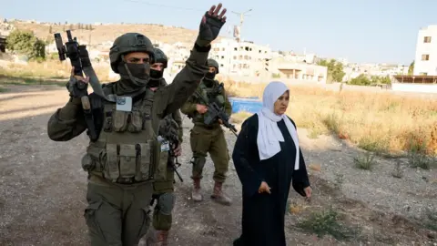 Reuters An Israeli soldier gestures as they prevent a Palestinian woman from reaching a cemetery in Jenin refugee camp, in the occupied West Bank (6 June 2025)