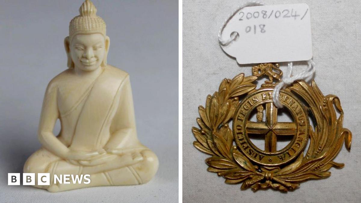 A carved ivory buddha with robes in a cross-legged position. It sits next to a circular belt buckle with a laurel motif with the words "Auspicio Regis et Senatus Angliae".