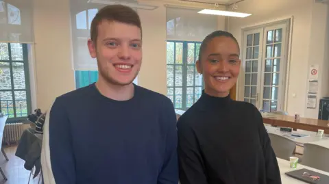 Students Alexandre Hubert and Valentine Guillot smile at the camera while standing in a classroom