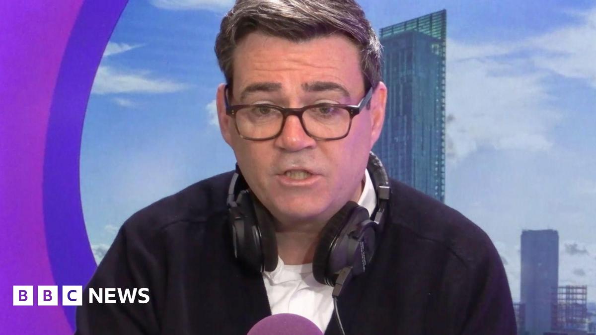 Andy Burnham gestures with his hands held at shoulder width as he gives a speech while wearing a black top.