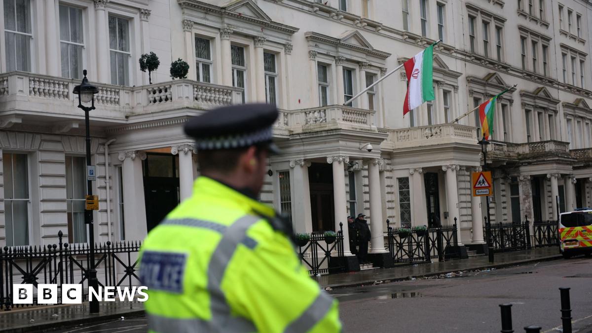 A police officer, dressed in a fluorescent yellow police jacket faces towards the Iranian embassy building in London.