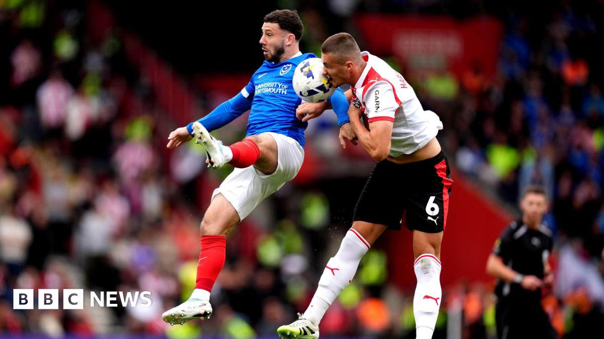 Portsmouth's Conor Chaplin battles for possession of the ball in the air with Southampton's Taylor Harwood-Bellis. Both men are captured vying for the ball in midair with Harwood-Bellis managing to get his head on it.