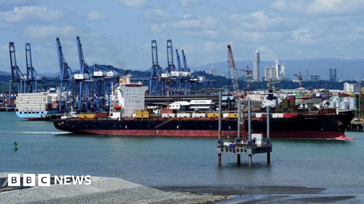 A large black and red container ship sails near the Balboa Port, as other container ships and cranes are seen in the background
