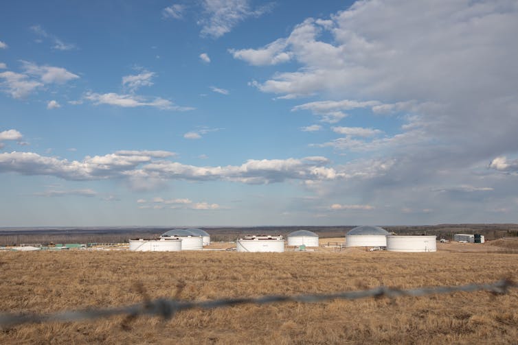 Several low white buildings on a Prairie field under a blue sky photographed from a distance.