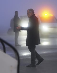 A thin man is seen in profile at dusk getting into a plane