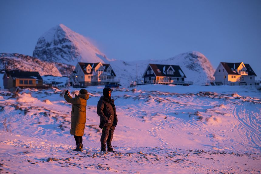 Locals stand on a snowy shoreline at dusk in Nuuk, Greenland, on January 21.