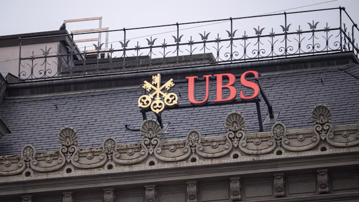 The UBS logo in gold and red is displayed atop the ornate facade of the former Credit Suisse headquarters.