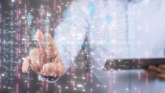 A person interacts with a virtual projection displaying digital human icons and data visualizations, representing artificial intelligence.