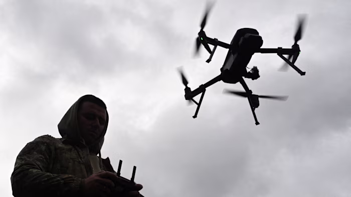 A Ukrainian serviceman in camouflage operates a drone with a remote control under a cloudy sky.