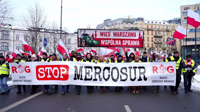 Polish farmers wearing yellow vests hold a large banner reading ‘Stop Mercosur’ and wave Polish flags during a street protest.