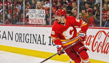 Calgary Flames defenseman MacKenzie Weegar skating with the puck along the boards during a game. Behind the glass, a smiling blonde fan holds up a handwritten white sign that reads, "GOOD LUCK IN OTTAWA MACKENZIE!", referencing trade rumors connecting him to the Ottawa Senators.