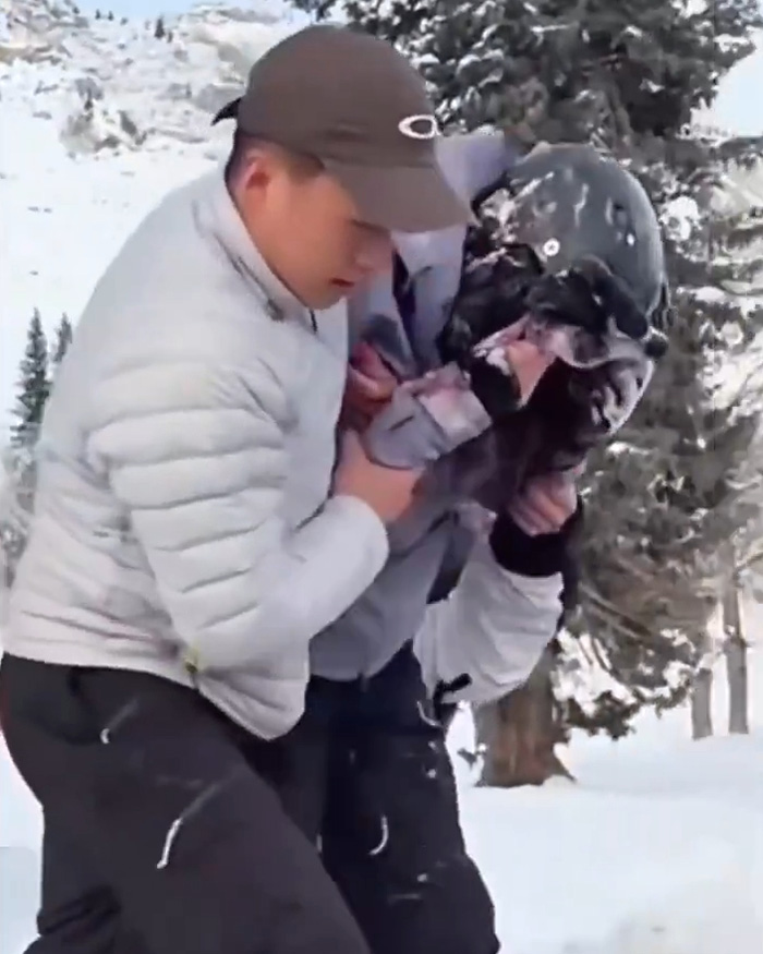 Man in winter gear helping injured skier during snow leopard attack in snowy forest setting after attempting selfie.