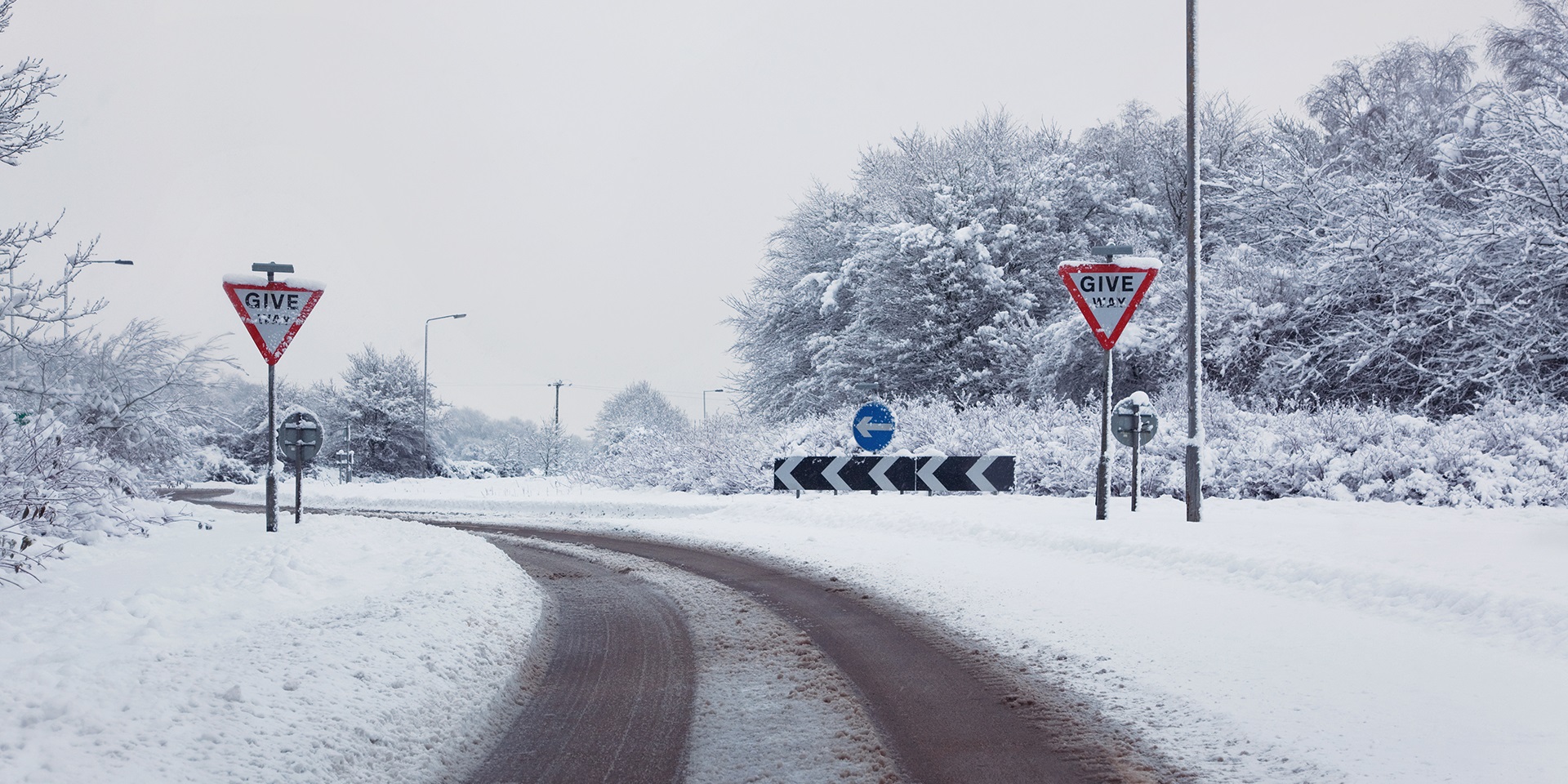 A snowy, bendy country road with traffic signs.