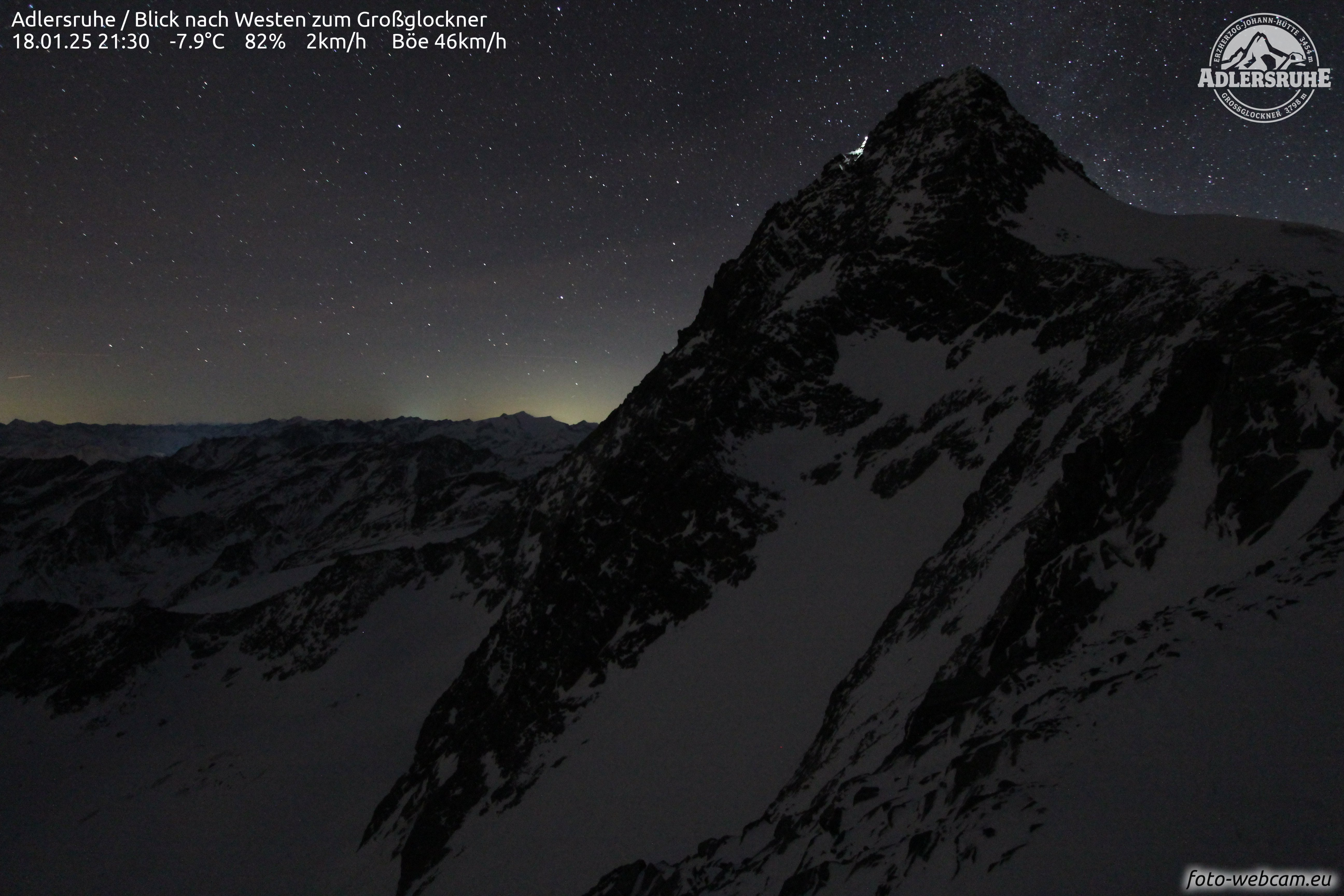 Nighttime webcam footage shows a snow-covered mountain peak under a starry sky.