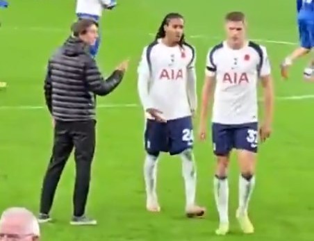 Tottenham Hotspur players Djed Spence and Micky Van de Ven walk away as their manager Thomas Frank gestures towards them on the field.