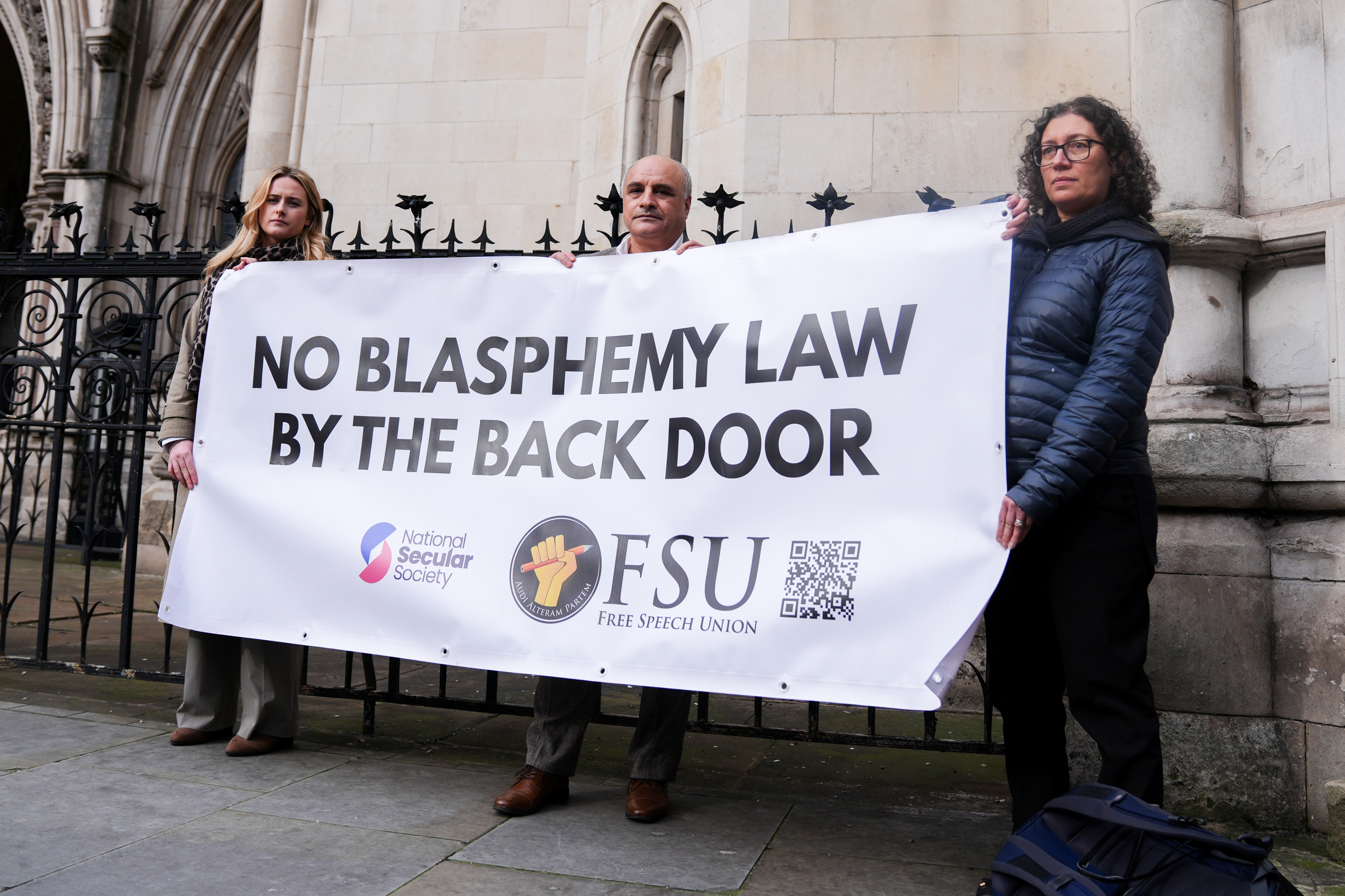Hamit Coskun and supporters hold a banner that reads "NO BLASPHEMY LAW BY THE BACK DOOR" outside the Royal Courts Of Justice.
