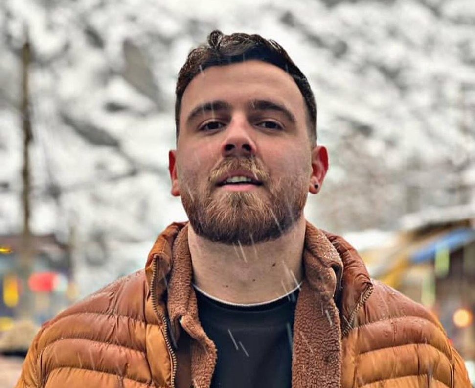 Erfan Soltani, a man with a beard, wearing a brown puffer jacket and a black shirt, with snow falling around him.