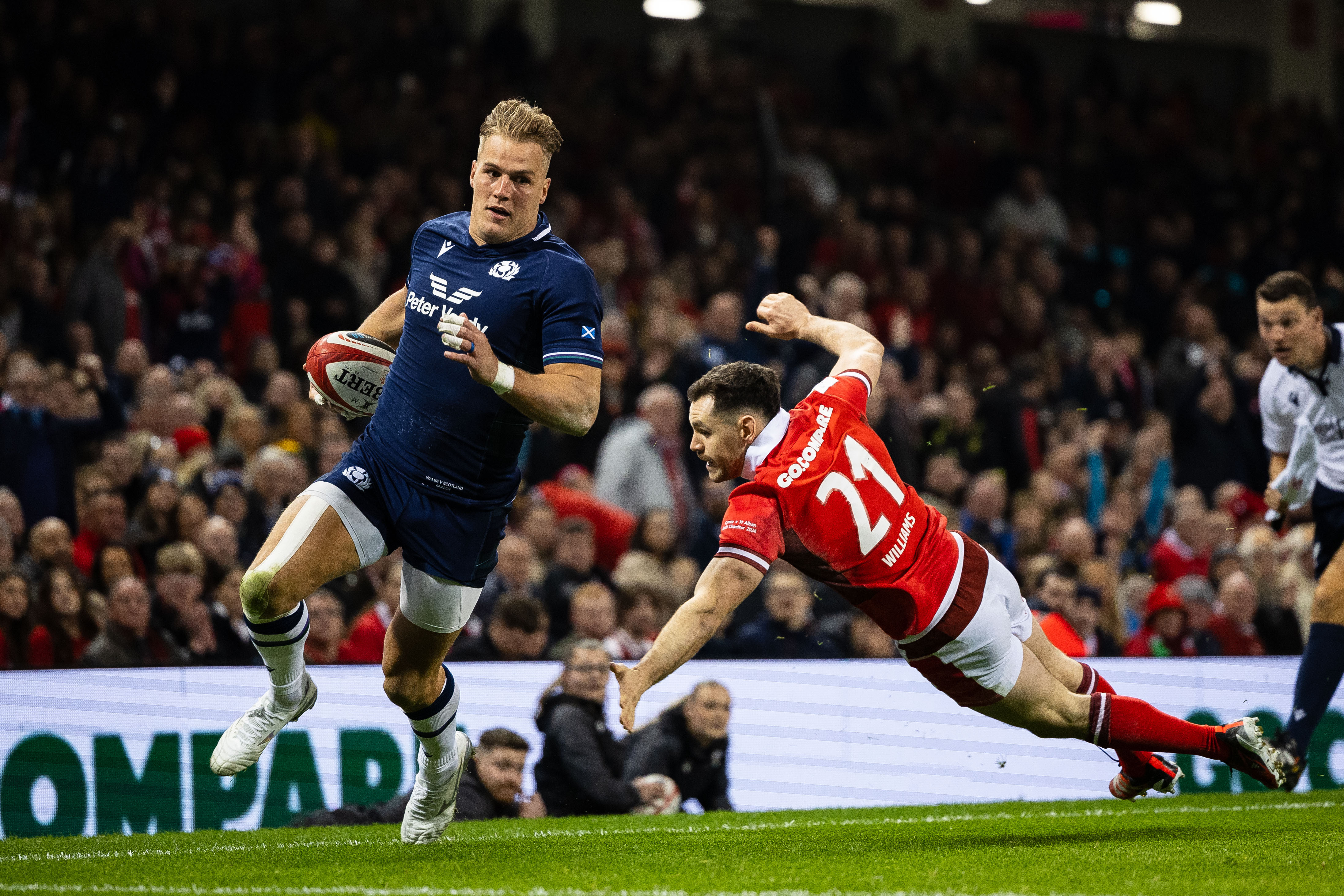 Duhan van der Merwe of Scotland runs with the ball while Tomos Williams of Wales attempts a tackle during a rugby match.