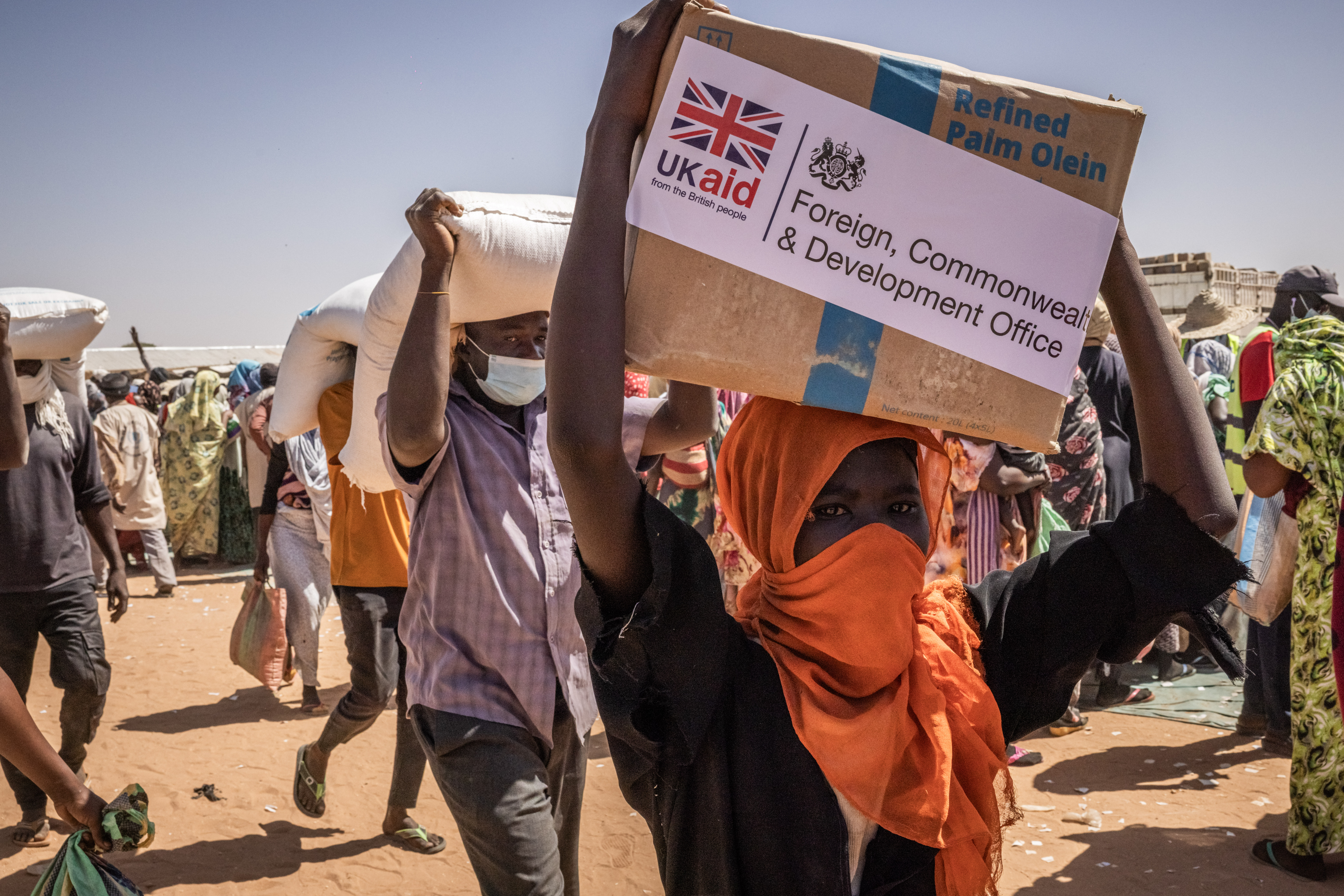 A young refugee in Chad carries a box of refined palm olein from UKaid and the Foreign, Commonwealth & Development Office during a food distribution.