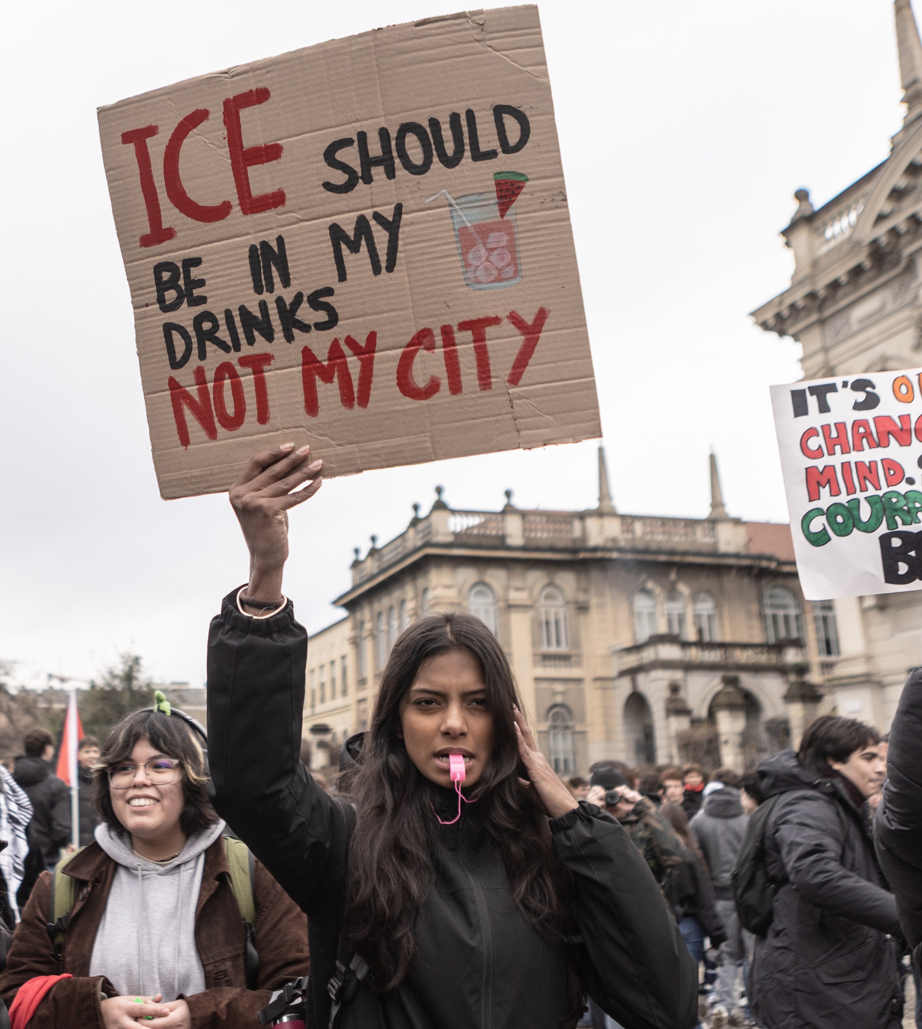 A woman holding a sign that reads "ICE should be in my drinks, not my city" at a protest against ICE's presence in Milan.