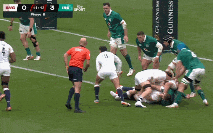 Rugby players from England and Ireland forming a ruck, with a referee and other players nearby.