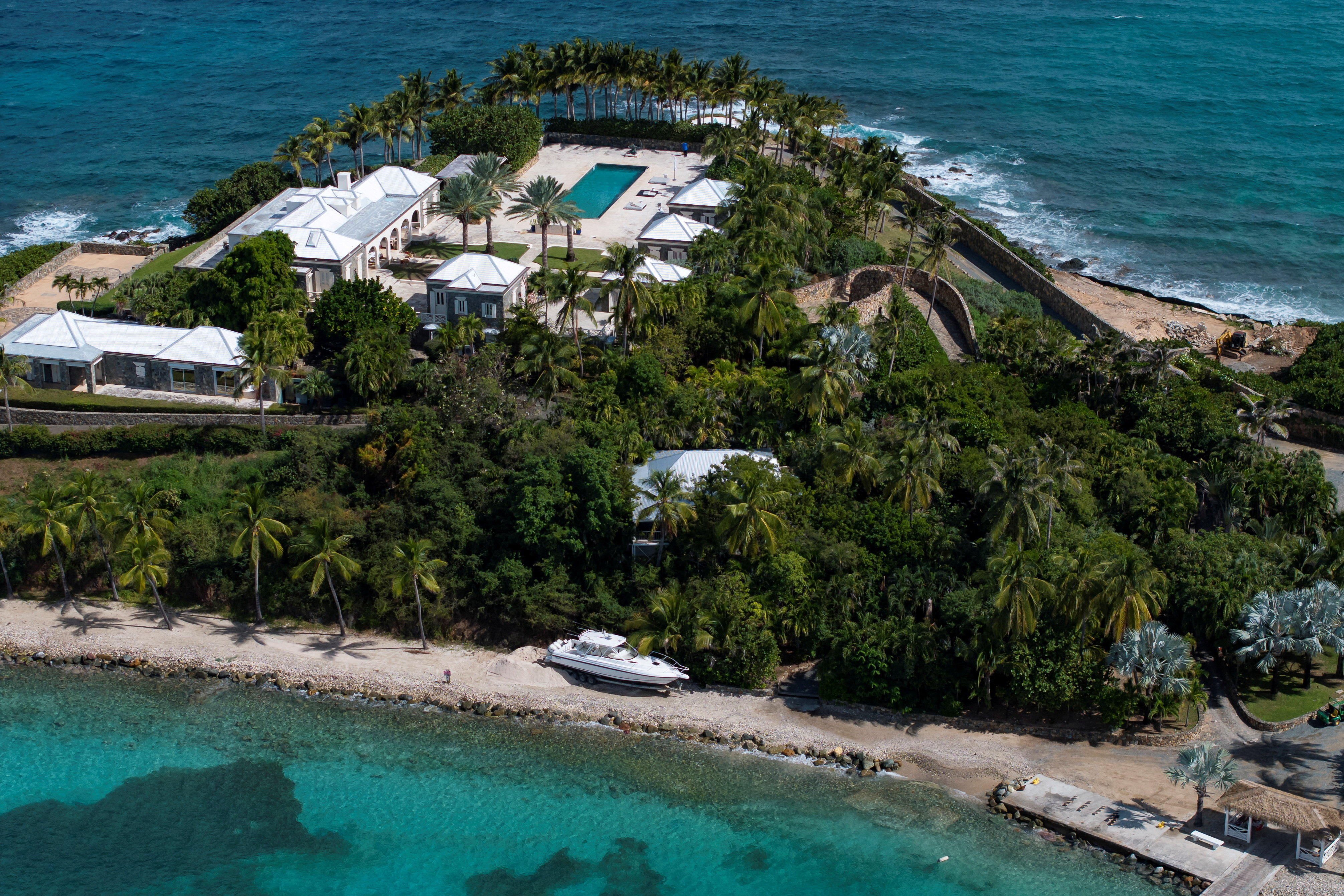 Drone view of Little St. James island with a pool, multiple buildings, and lush foliage surrounded by turquoise water.