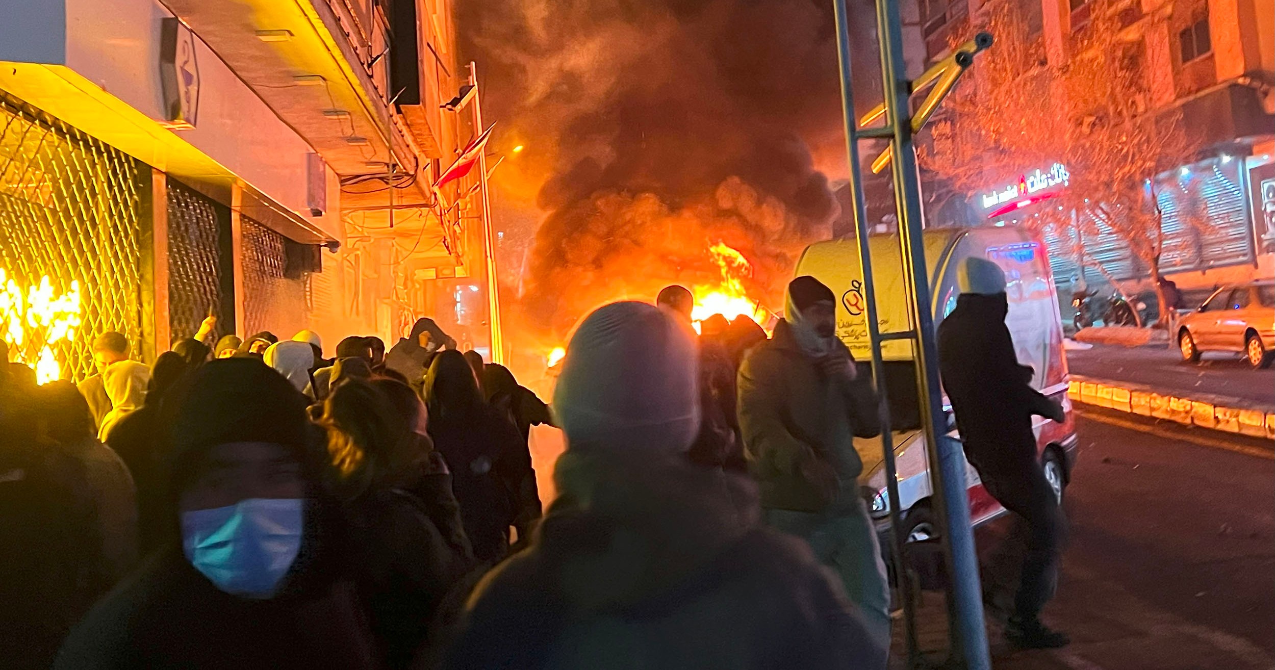 Protesters on Karimkhan Street in Iran amidst fire and smoke.