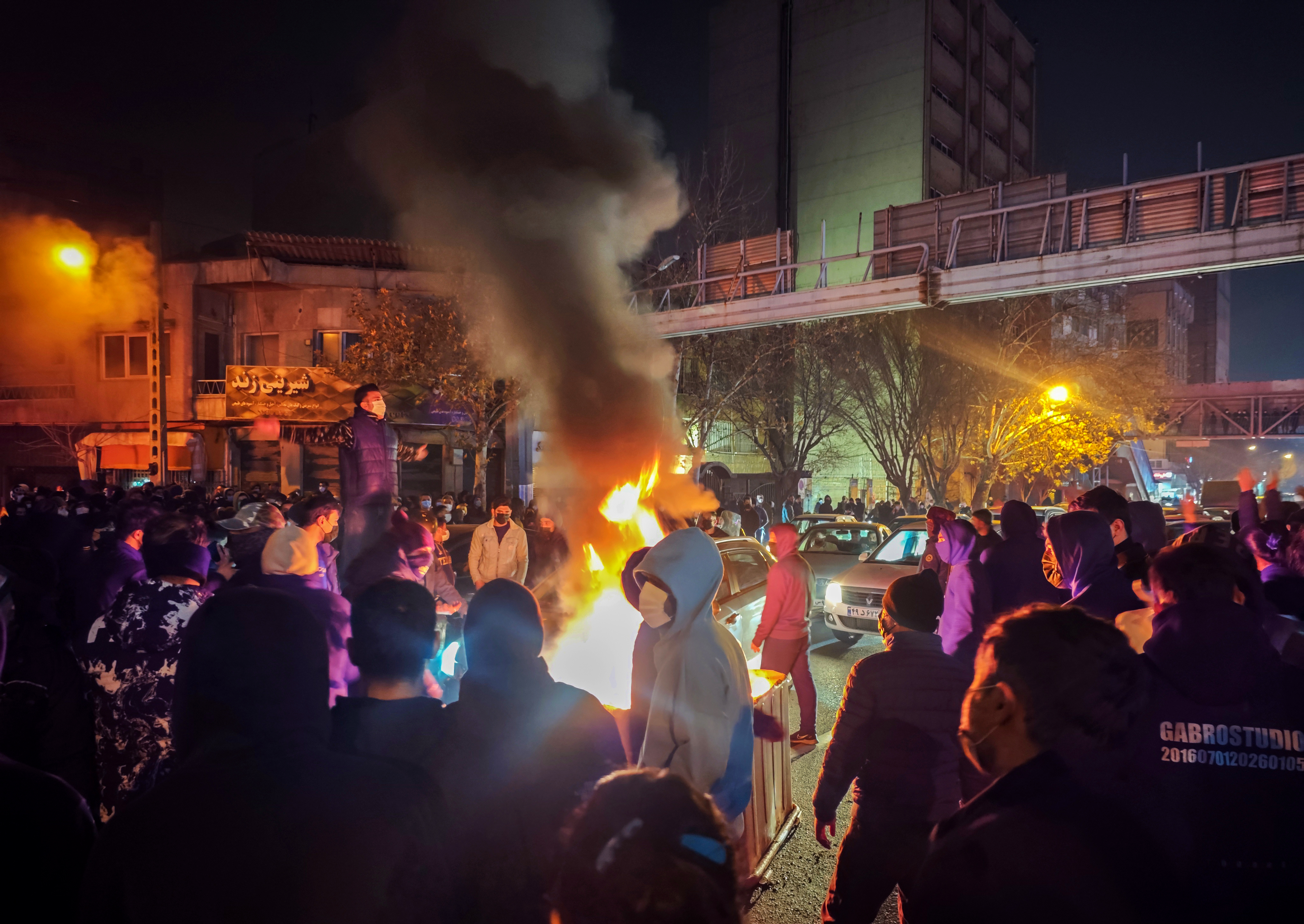 Protesters rally at night in Tehran, Iran, with fires lit in the street.