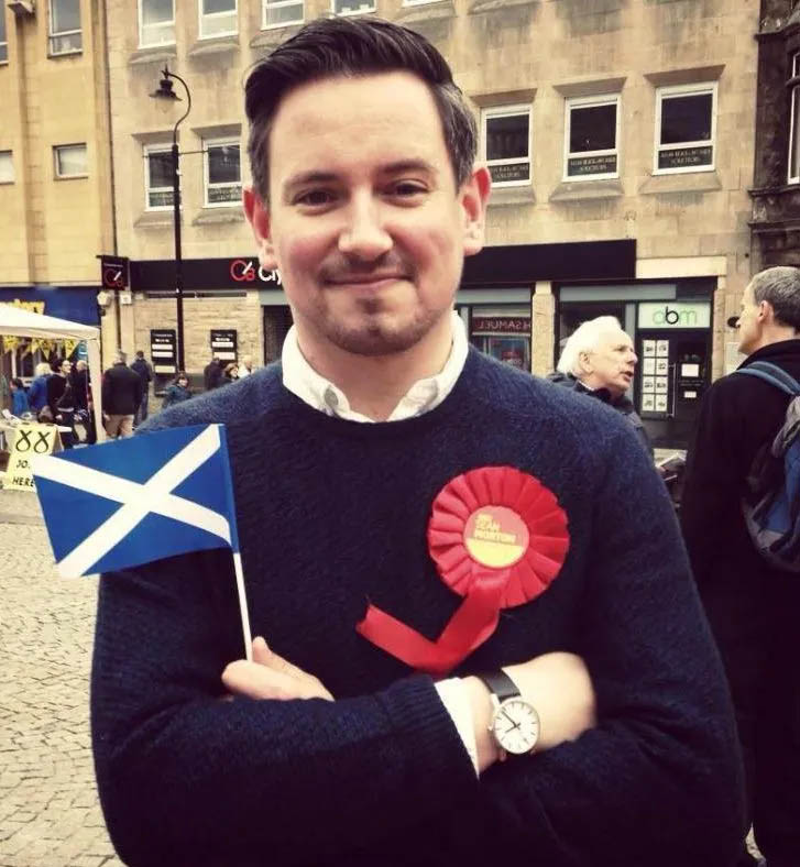 Sean Morton, Moray councillor, wearing a red rosette and holding a Scottish flag.