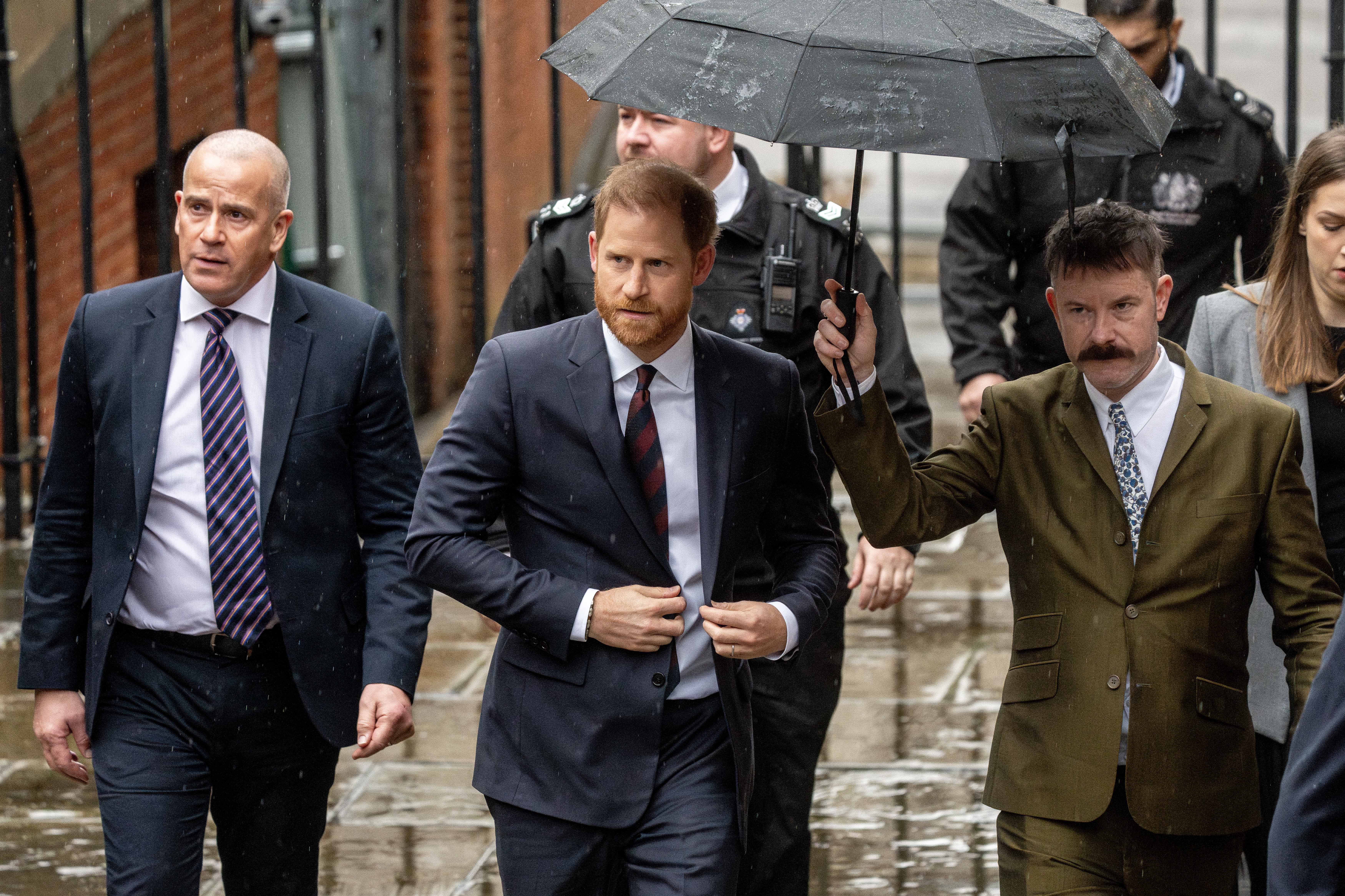 The Duke of Sussex arrives at the Royal Courts Of Justice, accompanied by other individuals, one holding an umbrella.