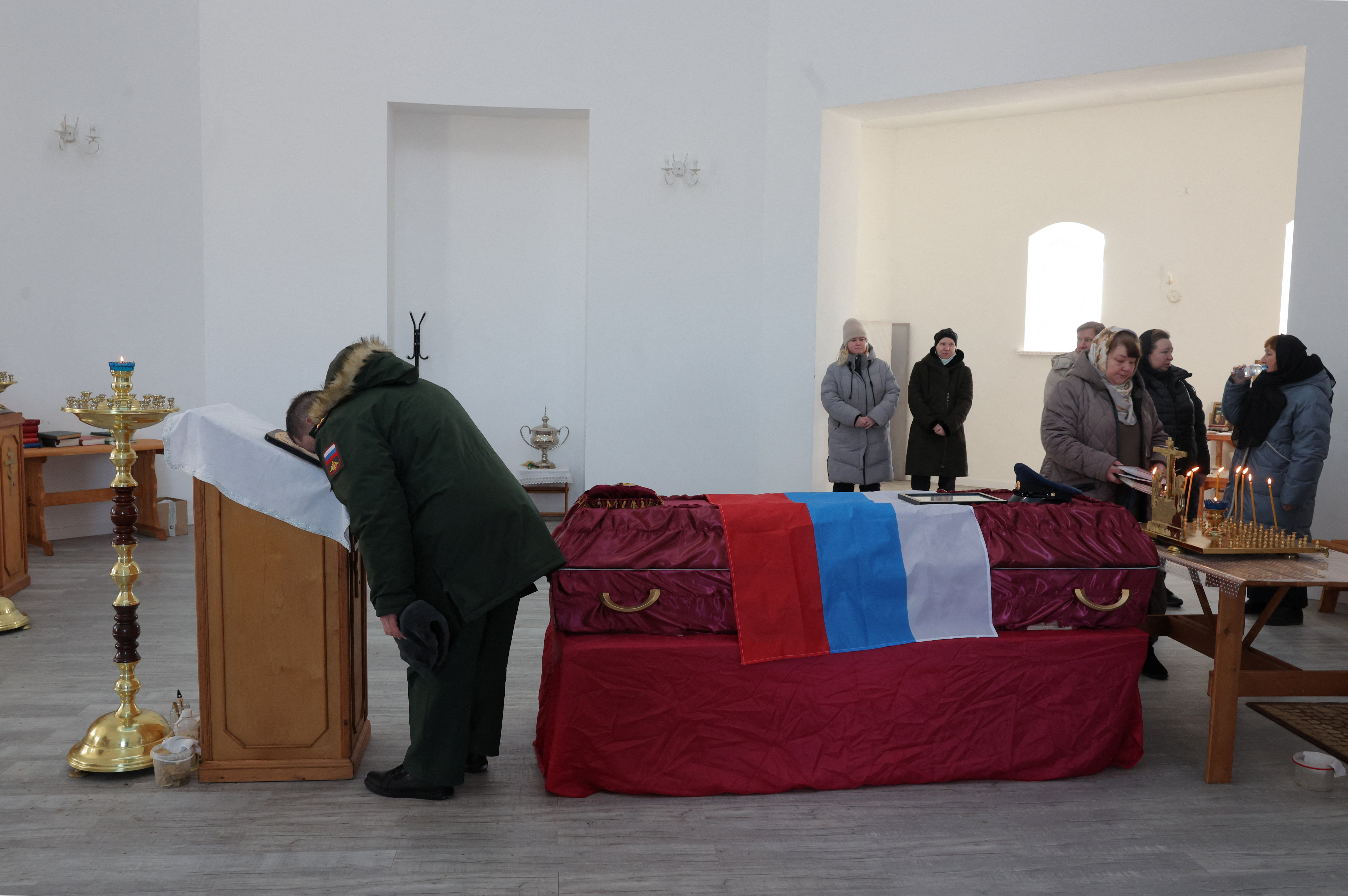 Mourners gather around a coffin draped with the Russian flag during the funeral of a Russian soldier killed in the Russia-Ukraine conflict.