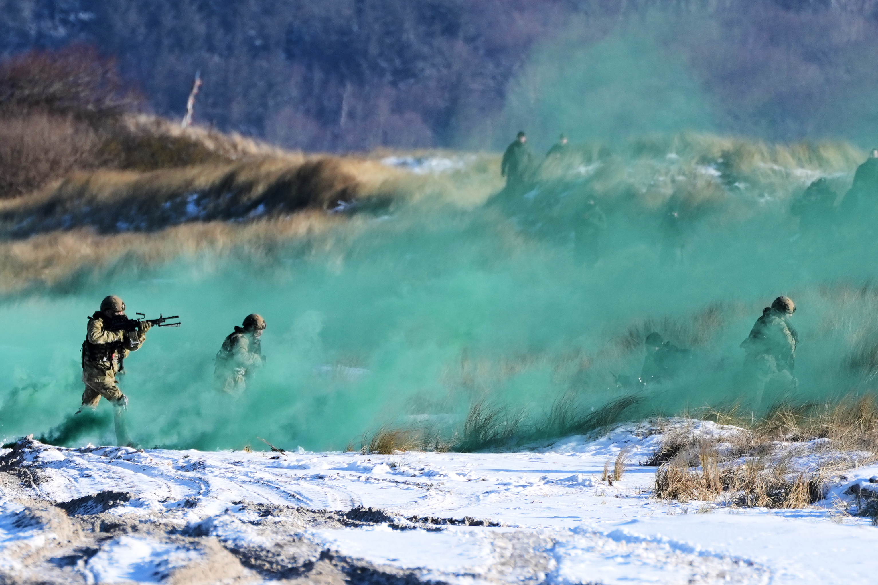 Soldiers perform an amphibious landing during NATO exercises on a beach covered in green smoke.