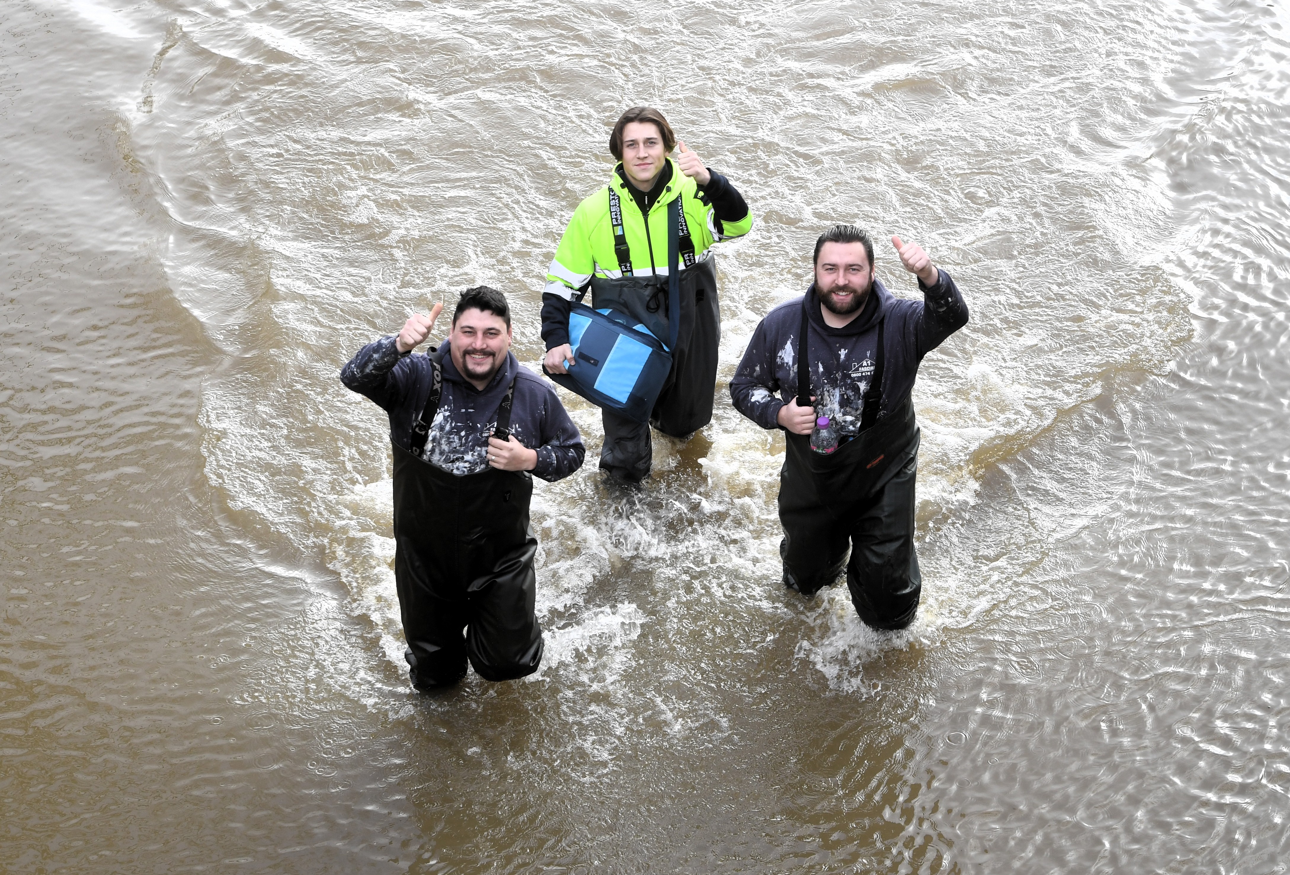 Three men in waders giving thumbs up in floodwater on Sandhurst Lane.