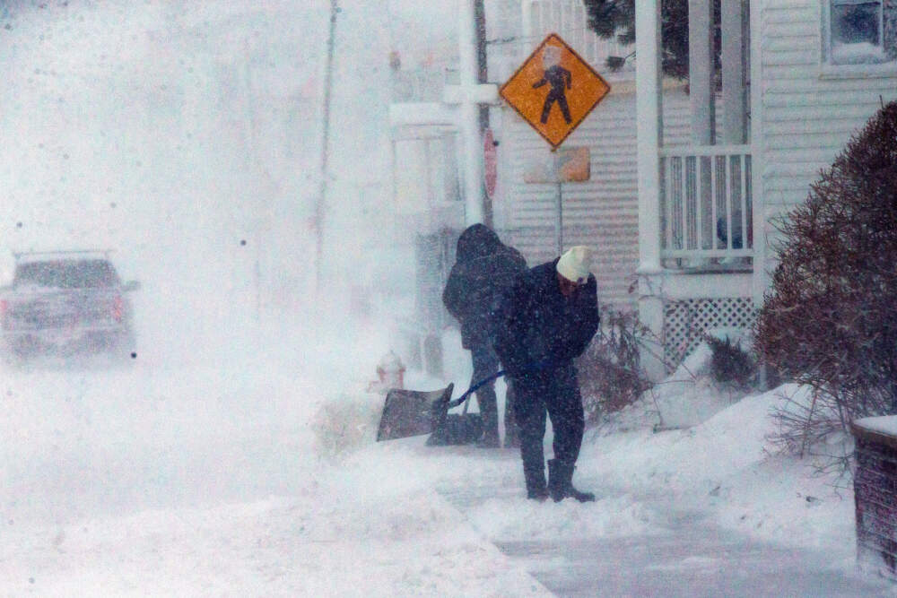 Two men shovel the sidewalk on Winthrop Shore Drive as they get pounded by the high winds and snow of the nor’easter. (Jesse Costa/WBUR)