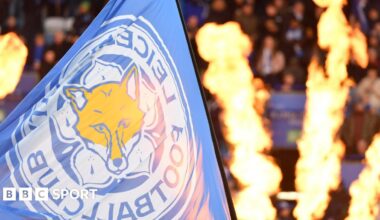 A flag with Leicester City's logo being waved, with pyrotechnic flames in the background
