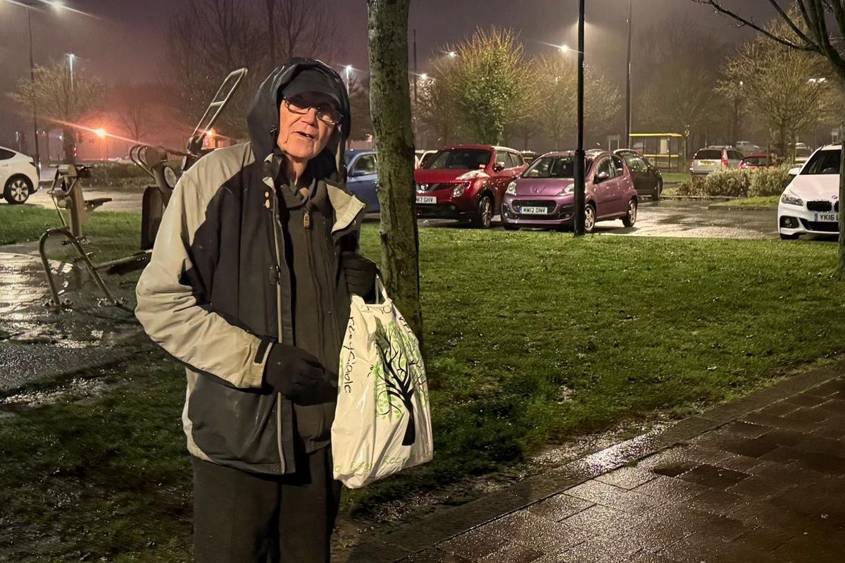 An old man carrying a shopping bag on a rainy night