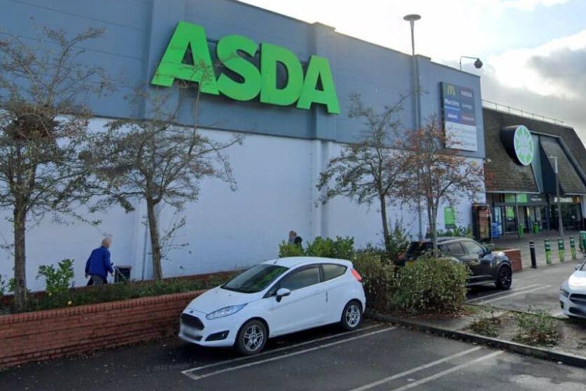 An exterior view of an Asda store with a white car parked in front, showcasing the building's modern architectural design and greenery.