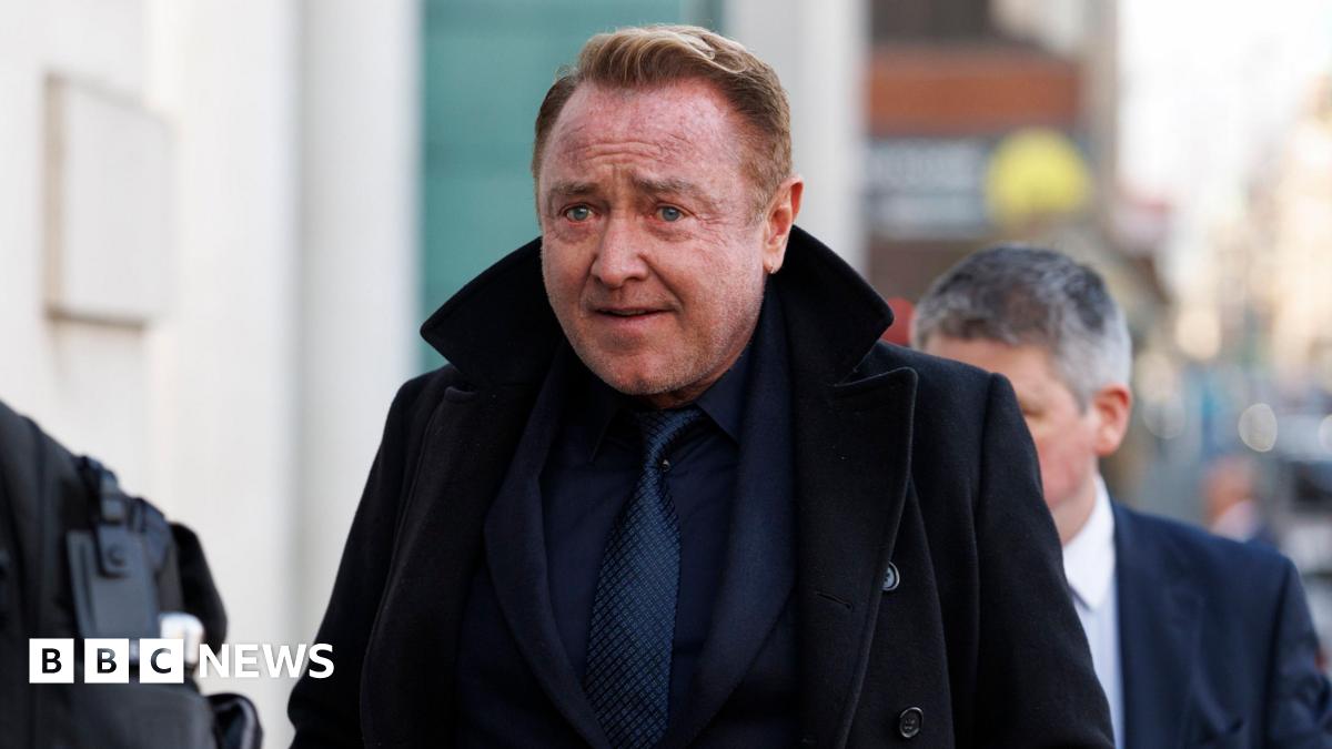 Michael Flatley. He has short reddish hair, wearing a navy suit and black coat.