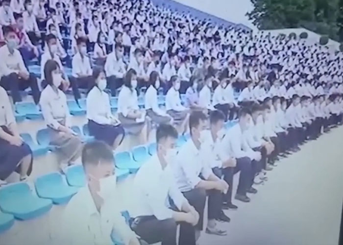 Large group of North Korean citizens wearing masks seated in rows outdoors amid reports of public executions for watching Squid Game.