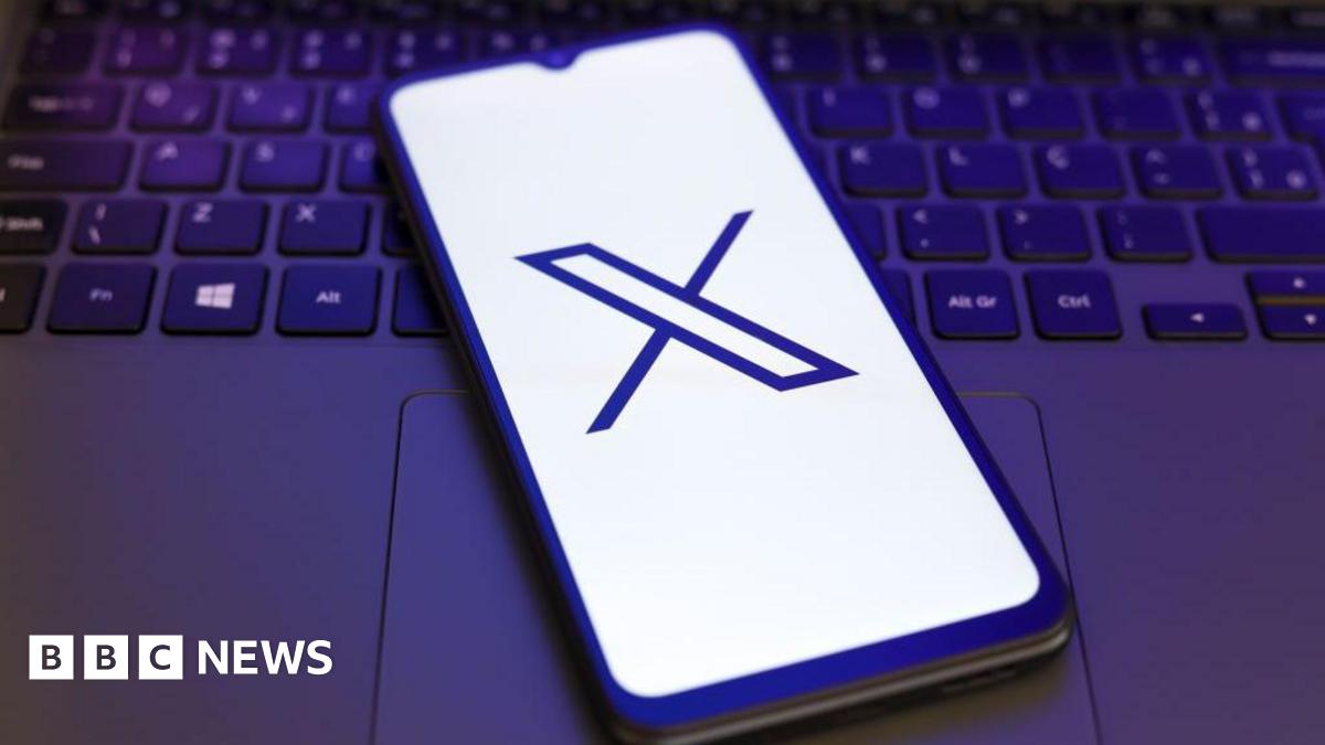 X logo displayed on a smartphone lying on a laptop keyboard