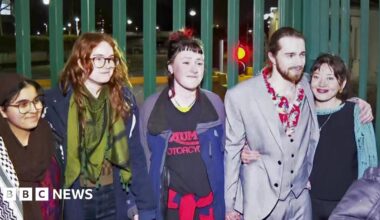 Charlotte Head, Leona Kamio, Fatema Rajwani, Zoe Rogers and Jordan Devlin standing outside in the dark with a green, metal fence behind them. They are smiling.