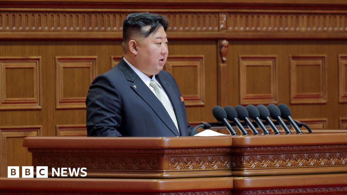 Kim Jong Un speaking at a podium, wearing a black suit.