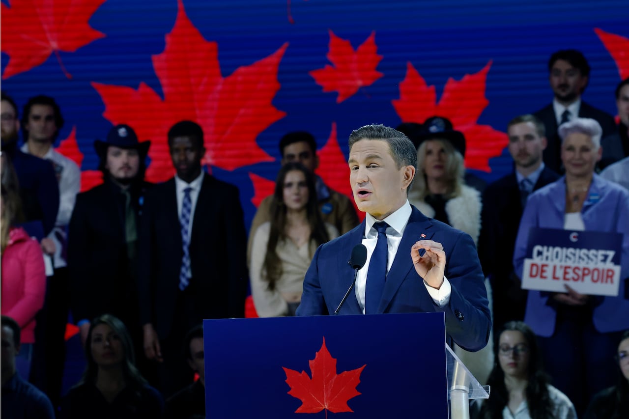 A man in a blue suit speaks at a podium with several others standing behind him.
