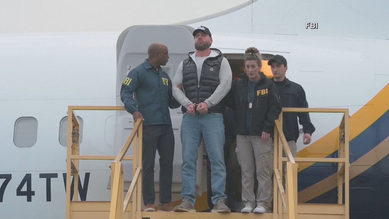 A bearded man is walked out of a plane by FBI agents